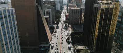 An aerial daytime view of Paulista Avenue in São Paulo, Brazil, showing heavy traffic and modern corporate skyscrapers.