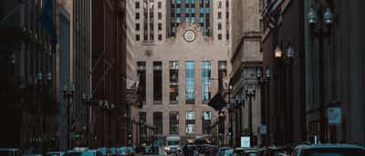 The historic facade of the Chicago Board of Trade building viewed down the center of a busy urban canyon.