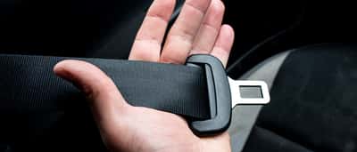A close-up of a hand holding a black car seatbelt across a dark interior.