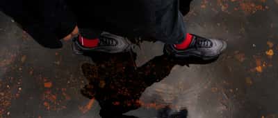 A person wearing Nike sneakers steps into a dark puddle that reflects their silhouette.