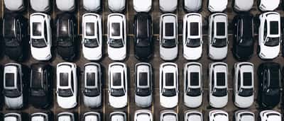 An aerial view shows hundreds of new cars neatly arranged in rows in a massive factory parking lot.