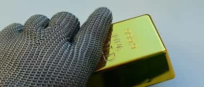 A hand wearing a metal chainmail glove holds a shiny gold bar.