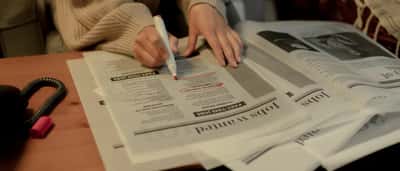 A person uses a pink marker to highlight job listings in the classifieds section of a newspaper.