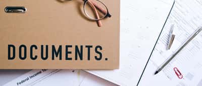 A folder labeled 'DOCUMENTS' rests on a desk next to a printed calendar, paperwork, and eyeglasses.