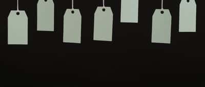 Multiple blank cardboard price tags hang from strings against a dark background.