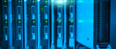 A metal server blade partially slid out of a glowing blue data center rack.