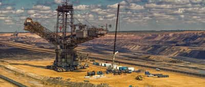 A massive bucket-wheel excavator operates in a vast open-pit mine under a cloudy sky.