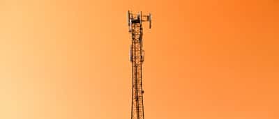 A telecommunications tower stands against a vibrant orange sky.