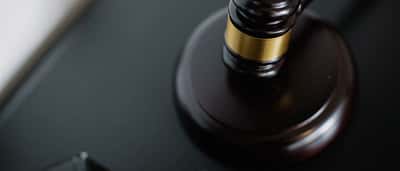 A close-up view from above of a dark wooden judge's gavel with a gold band resting on a black desk.