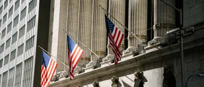 American flags hang between the sunlit columns of the New York Stock Exchange building.