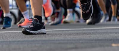 A close-up view of the feet and legs of multiple marathon runners moving along a paved road.