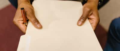 Close-up of a business professional in a suit holding a blank beige file folder and a pen.
