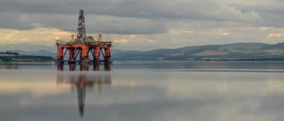 An offshore oil platform sits on a calm body of water beneath a dense, stormy sky.