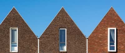 A row of contemporary brick houses with uniform pitched roofs under a bright blue sky.