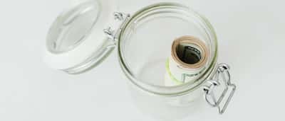 A roll of US dollar bills sits uninvested inside an open glass jar.