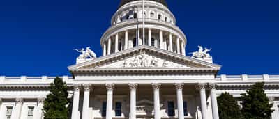 The white facade and dome of the California State Capitol building against a clear blue sky.