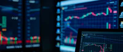 Glowing screens display fluctuating stock market charts and data in a darkened room.