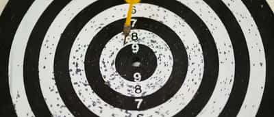 A single dart rests in the bullseye of a black and white target board.