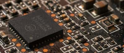 A moody, extreme close-up of a black microchip mounted on an intricate, shadowed circuit board.