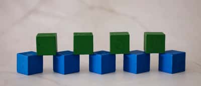 Blue and green wooden blocks arranged in an interlocking foundation pattern on a bright marble surface.