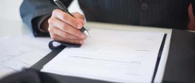 A close-up of a person signing a formal business document with a pen.