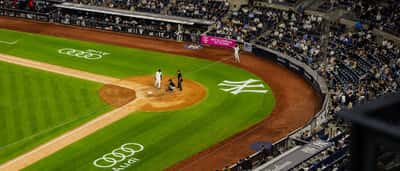 An aerial view of a baseball game underway at Yankee Stadium with the team logo visible on the field.