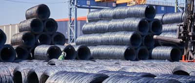 Massive stacks of steel wire coils stored outdoors at a bright industrial site.
