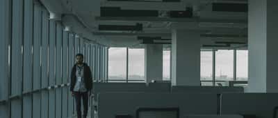 A single employee walks past rows of empty desks in a dimly lit office space.