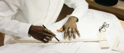Close-up of a professional's hands using a pencil and ruler to draft architectural blueprints.