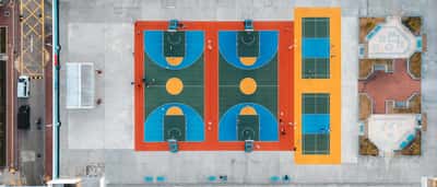An aerial, top-down view of brightly painted outdoor basketball courts with players seen from above.