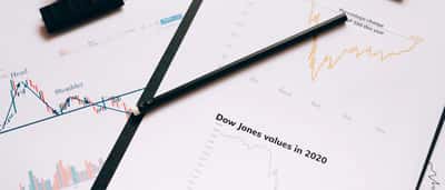 Printed financial charts displaying data for the S&P 500 and Dow Jones indexes lie on a desk with a pencil resting across them.