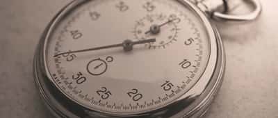A close-up of a vintage silver stopwatch resting on a textured surface in sepia tones.