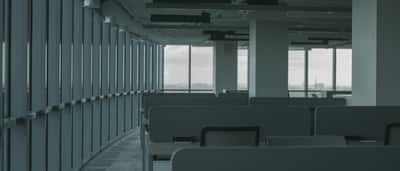 Rows of empty cubicles in a dimly lit, modern commercial office building with large glass windows overlooking a city.
