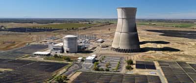 An aerial view of a nuclear power plant's cooling tower and reactor building surrounded by a field of solar panels.