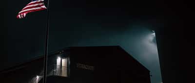 A large American flag is displayed on the side of the Stargate building at night.