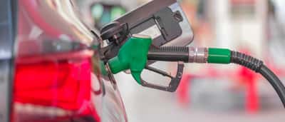 A green fuel pump nozzle fills a car at a gas station.