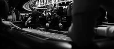 Black and white photograph of people placing bets around a casino craps table.