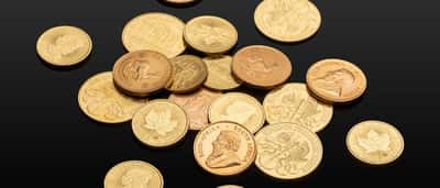 A collection of various physical gold coins scattered across a reflective black surface.