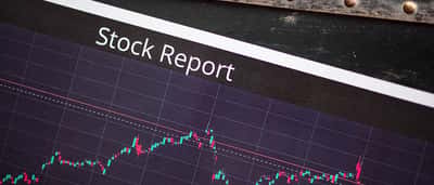 A document horizontally labeled Stock Report rests on a digital screen displaying fluctuating financial market charts.