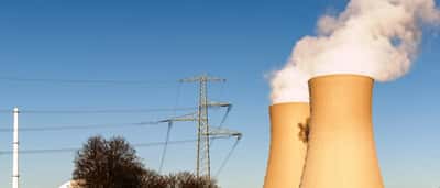 Cooling towers and high-voltage transmission lines of a power plant against a clear blue sky.
