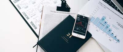 A high-angle view of a stock trading desk featuring printed financial charts and a smartphone displaying market trends.