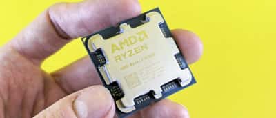 A hand holds an AMD Ryzen processor against a bright yellow background.