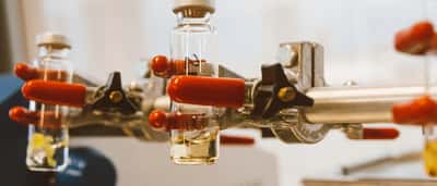 Glass vials held by red-handled metal clamps in a pharmaceutical research laboratory.