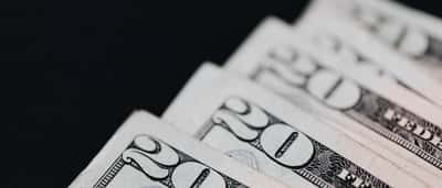 A macro shot of United States twenty-dollar bills neatly layered against a stark black background.