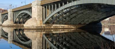 A sturdy stone and steel bridge spanning a calm river under a clear blue sky.