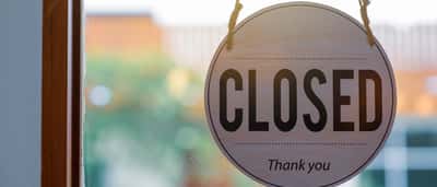 A round wooden closed sign hanging on the inside of a glass window or door.