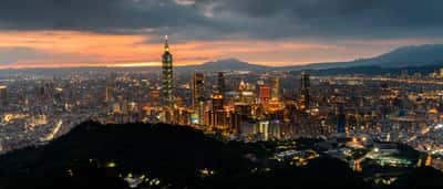 A sweeping view of the modern Taipei skyline at sunset, anchored by the towering Taipei 101 skyscraper.