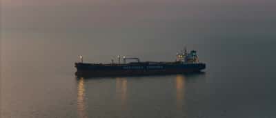 A solitary oil tanker ship sailing on calm ocean waters during twilight.