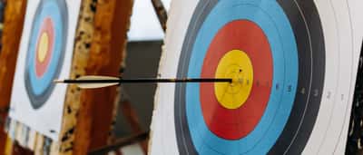 An arrow sits perfectly centered in the yellow bullseye of a colorful archery target.