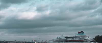 A large cruise ship anchored at port under a heavy, dramatic sky.